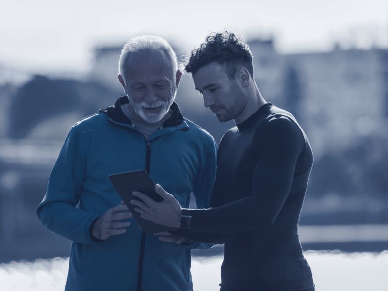 Deux hommes de générations différentes regardent ensemble la même tablette, dehors.