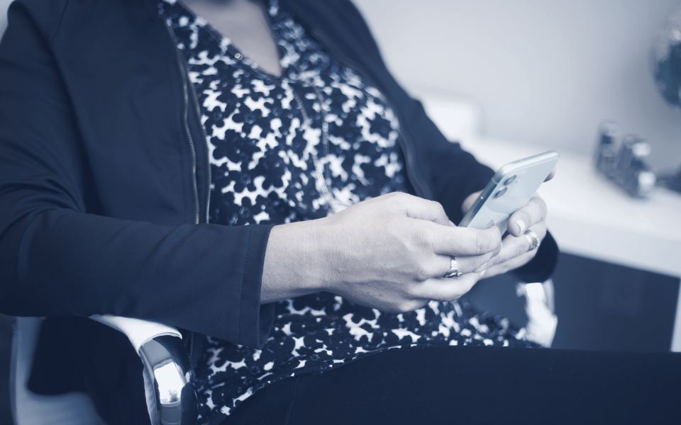Les deux mains d’une femme assise tiennent un téléphone, l’index posé sur l’écran.