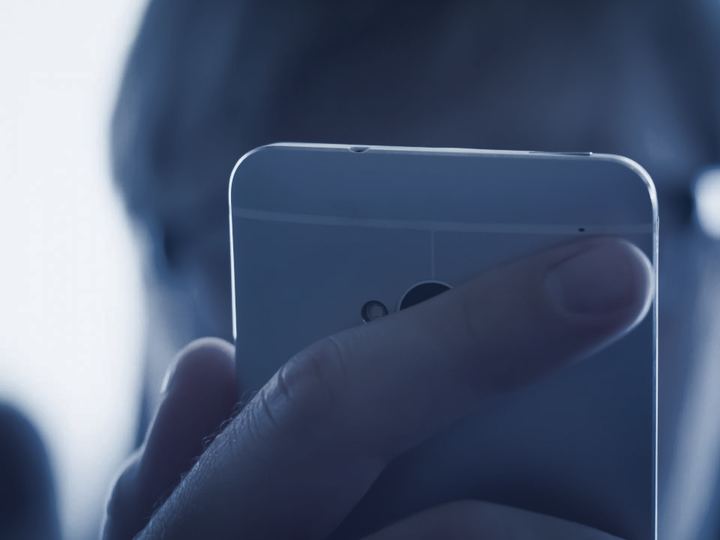 Gros plan sur un pouce qui approche le bord d’un téléphone, sans encore toucher l’écran.